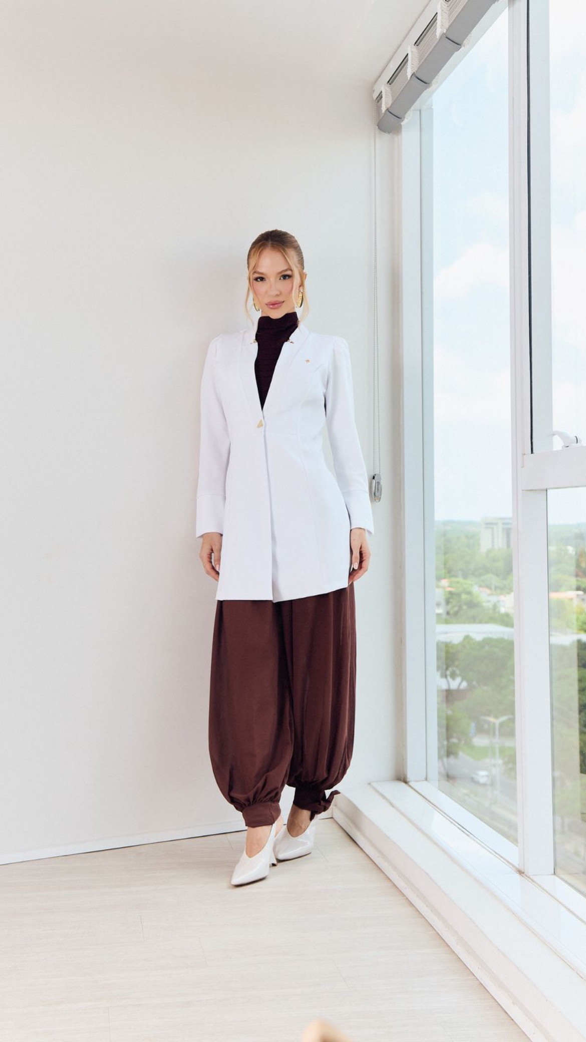Jaleco branco feminino com gola alta sobre calça marrom